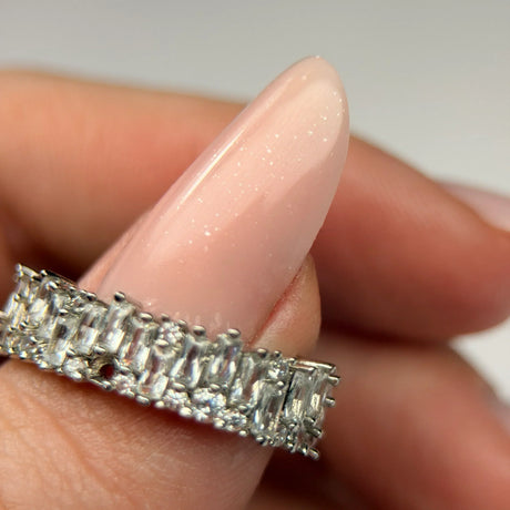 Jasnoróżowy paznokieć hybrydowy z delikatnym brokatem i srebrną biżuterią, stylizacja manicure